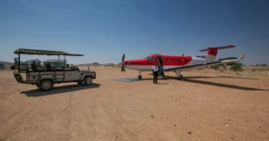 Red bush plane parked alongside open safari vehicle on Serengeti dirt airstrip.